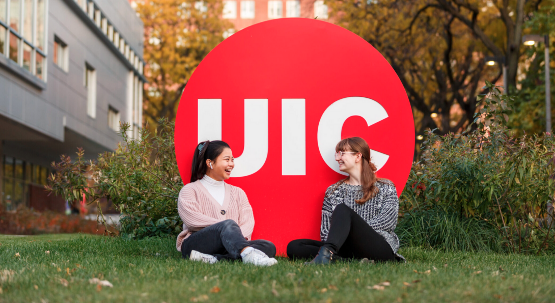 two women sitting on the grass in front of logo