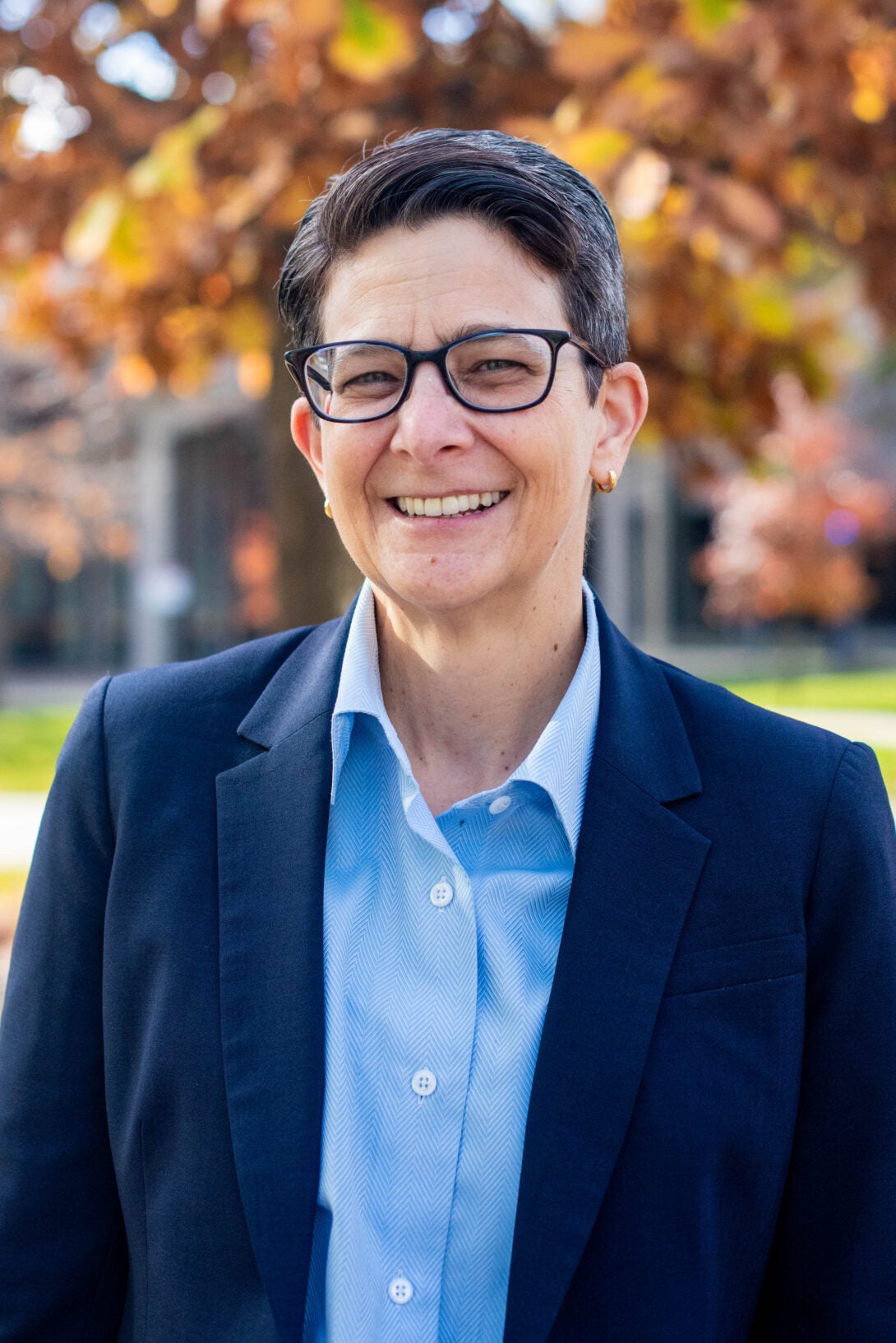 Lisa Freeman smiles in front of fall foliage on campus