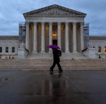 person walking with an umbrella in from of the supreme court 