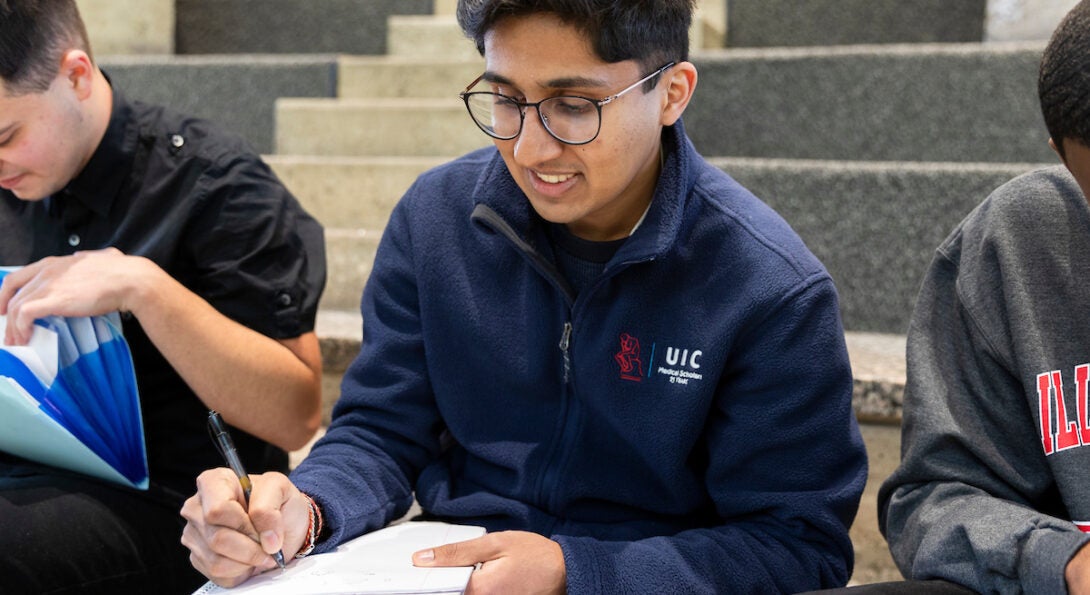 Young male Indian student takes notes in his notebook while sitting on a staircase.