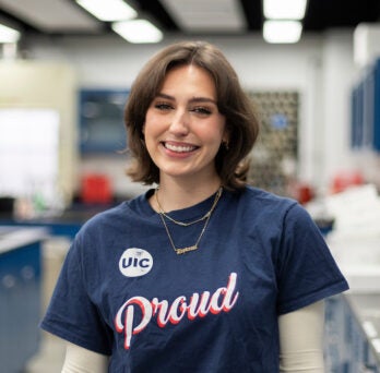 College of Liberal Arts and Sciences student Daytonna smiles in a lab. She is a young white woman with short brown hair, wearing a navy blue short sleeve shirt that says UIC Proud.
                  