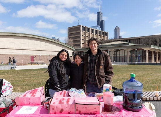 Two female students and one male stand on the University of Illinois Chicago's campus east quad under the Chicago skyline.