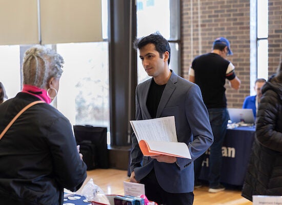 Young male student wearing dark gray blazer speaks to a woman at a career event.