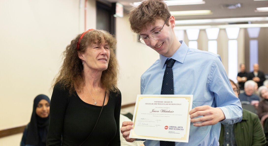 Student Jason Whitehair smiles down at his award certificate while his professor Janet Richmond smiles at him during ceremony.