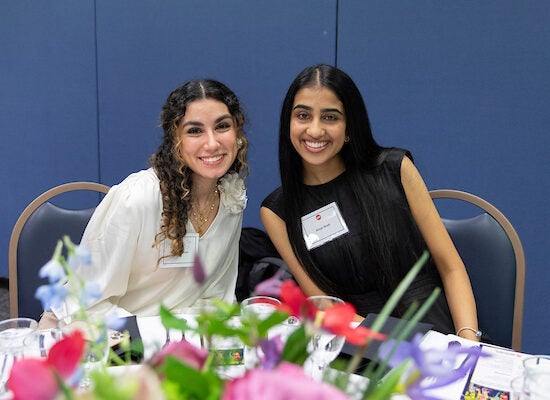 Two young female students lean together smiling at a scholarship event on the University of Illinois Chicago's campus.