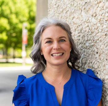 Academic Advisor Alexa Maseth stands smiling in front of a tan pebble stone column on University of Illinois Chicago's east campus.
                  