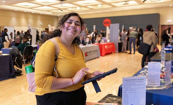 A student smiles and holds an iPad while filling out applications at UIC's spring career fair.