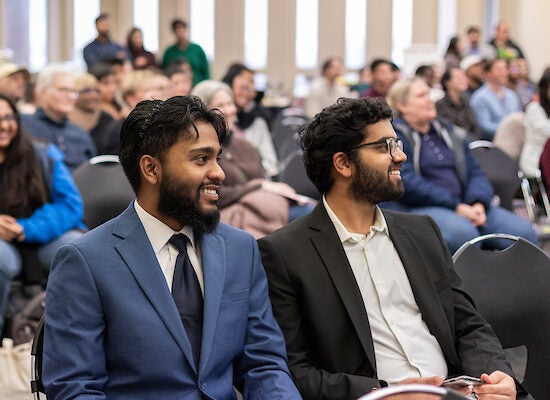 Two male students smile and wear suits at an award ceremony.