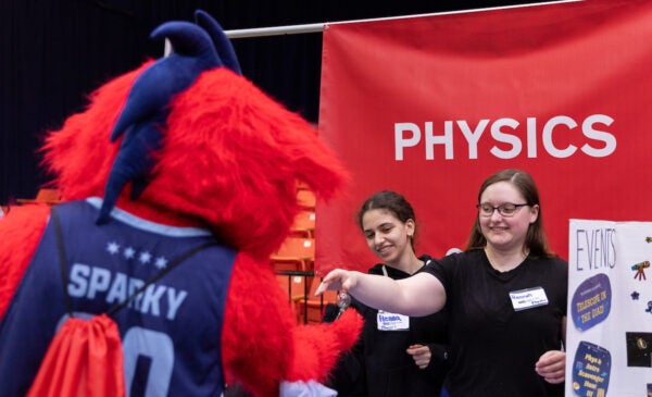 A student hands UIC's mascot Sparky a physics instrument.