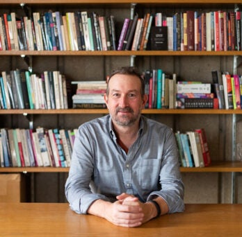 English Professor and Head of English Department Peter Coviello sits in front of his wall of books.
                  