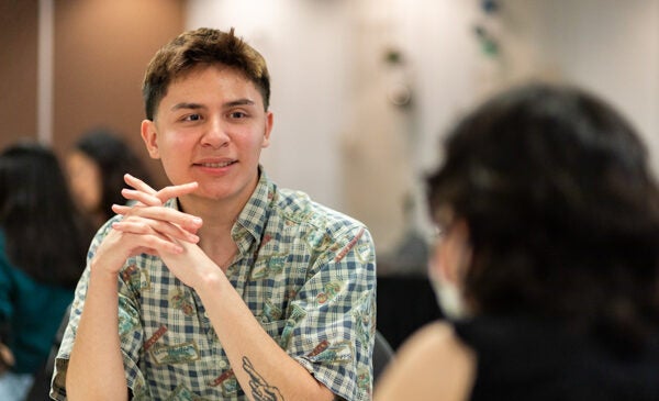 Young male student sits with his hands clasped at a table at an event.