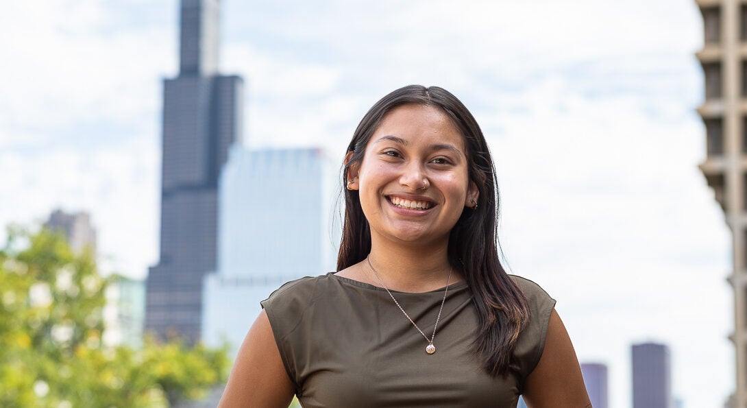 Student Jiselle Plata stands on UIC's campus with the Chicago skyline in the background