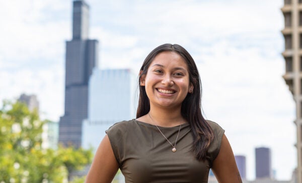 Student Jiselle Plata stands on UIC's campus with the Chicago skyline in the background