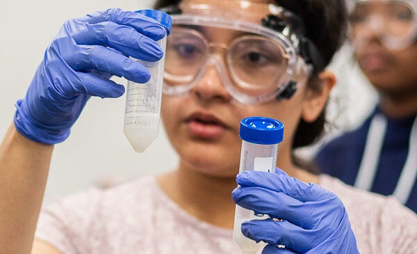 Student wearing goggles looking through test tubes in lab