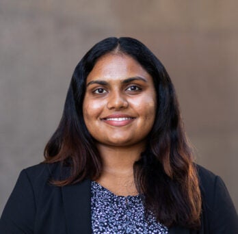 Student Ananya “Anna” Ramesh wearing a black blazer and floral shirt against brown background
                  