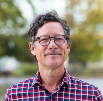 UIC Professor Christopher Grimes wearing checkerboard shirt stands on campus
                  