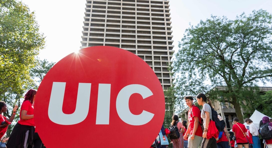 UIC Red Dot Logo on campus with students walking on a sunny day