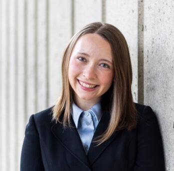 LASURI Student Isabel Kapustka wearing a blue button up shirt and navy blazer
                  