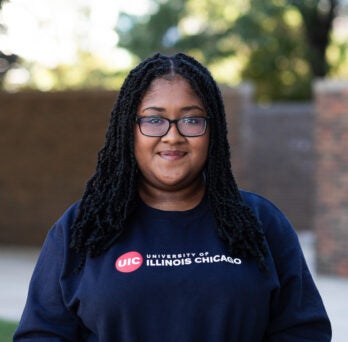 Student Kalya Pilgrim wearing glasses and blue crewneck sweatshirt on UIC's campus
                  