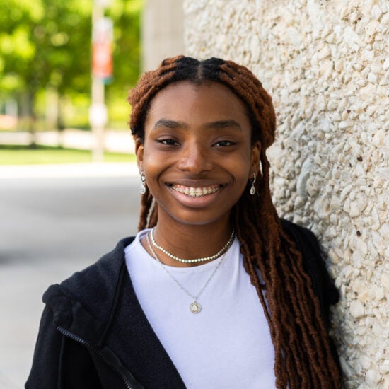 Psychology student at UIC stands on campus wearing white t shirt and black hoodie