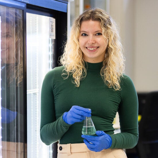 Biological Sciences student Iza Kopez in green sweater wearing blue rubber gloves in lab on UIC's campus