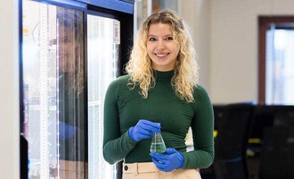 Biological Sciences student Iza Kopez in green sweater wearing blue rubber gloves in lab on UIC's campus