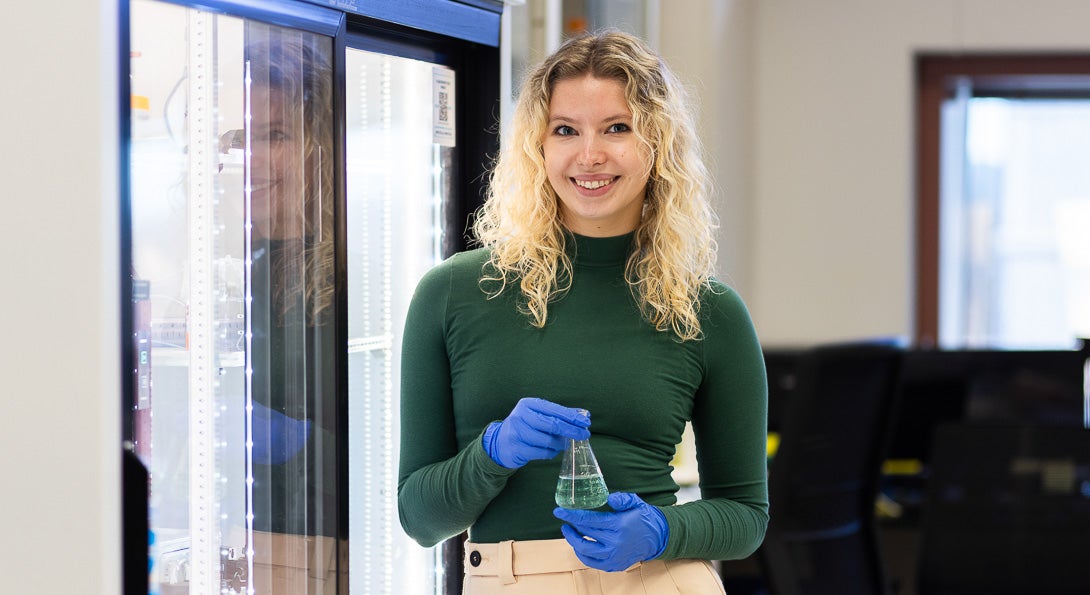 Biological Sciences student Iza Kopez in green sweater wearing blue rubber gloves in lab on UIC's campus