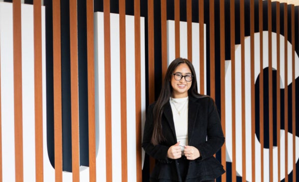 UIC Student Samantha Bravo standing in front of wooden logo sign wearing black blazer and white shirt