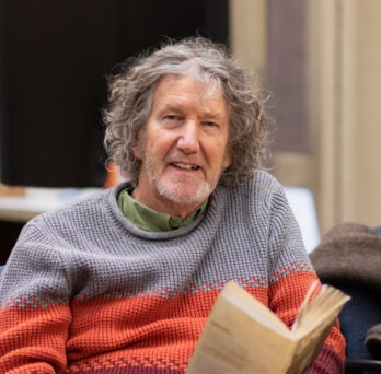 Professor Dave Schaafsma sits reading a book at a table in his office
                  