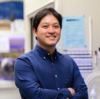 Professor Andy Nguyen in blue button down shirt standing in a lab
                  