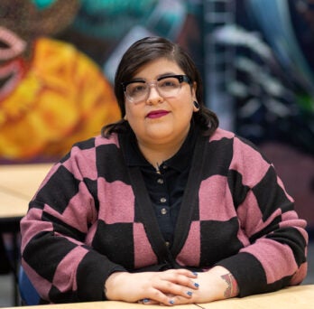 Liliana sits in the Latino Cultural Center in a black and pink checkered sweater
                  