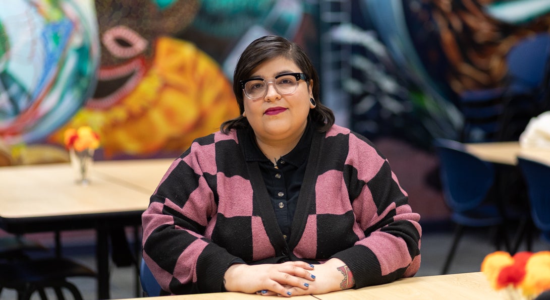 Liliana sits in the Latino Cultural Center in a black and pink checkered sweater