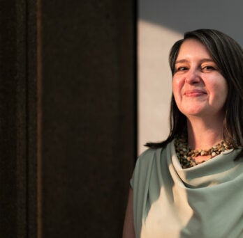 Anna Kornbluh stands in a dark room with sunlight falling onto half of her face
                  