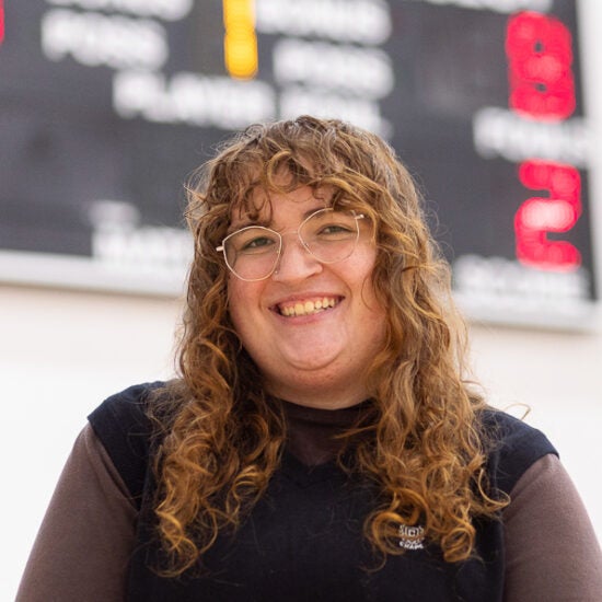 Communication major Piper Howard stands on basketball court with scoreboard behind her head